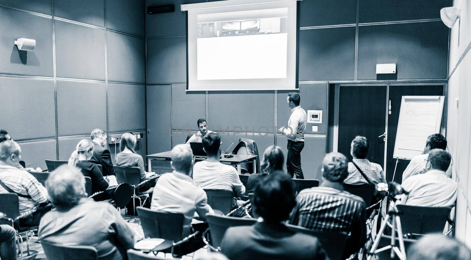 Speaker giving a talk in conference hall at business event. Unrecognizable people in audience at conference hall. Business and Entrepreneurship concept. Blue toned black and white.