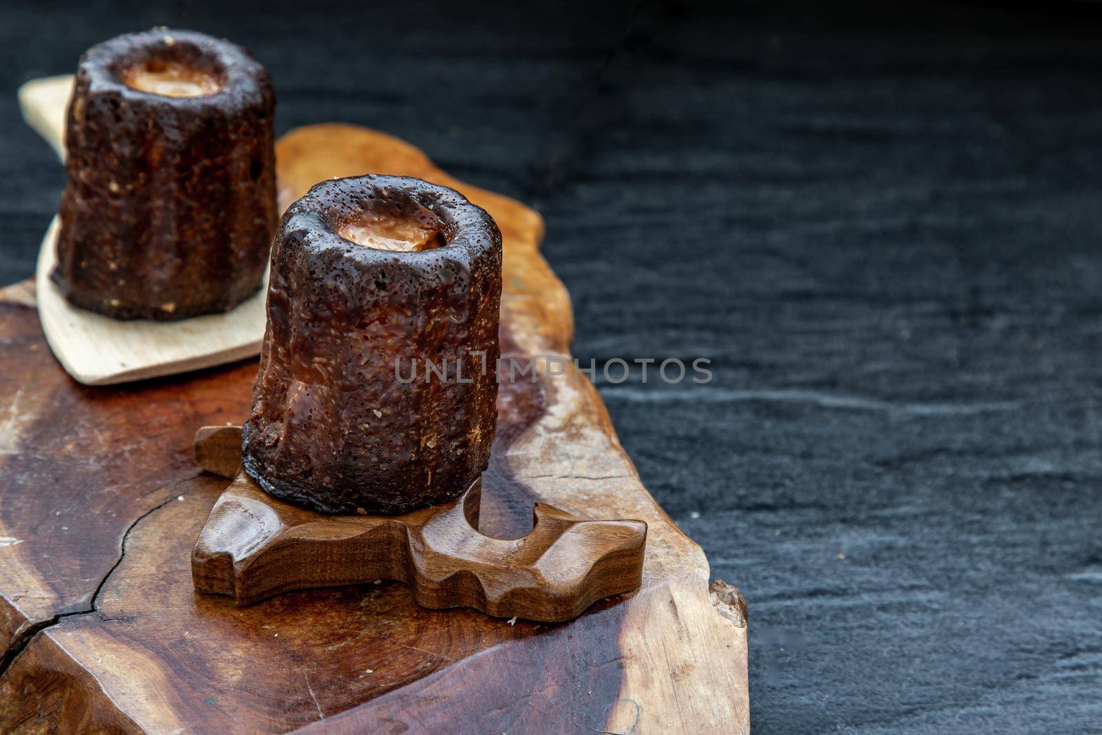 Cannelés (Canelés) de Bordeaux Recipe is a small pastry with rum and vanilla on a wooden plate. Traditional French sweet dessert. tasty snacks. Oblique view from the top. Place for text.