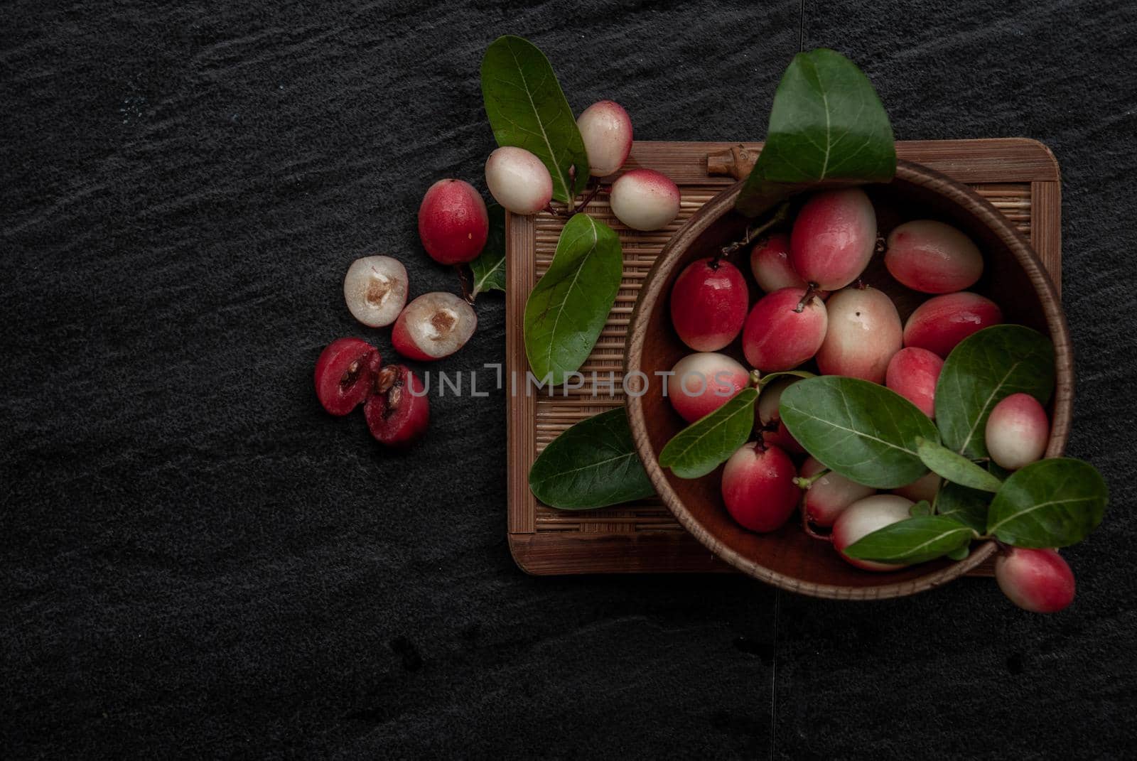 Bengal-Currants, Carandas-plum or Karonda fruit (Carissa carandas L.) sour taste fruit in Wooden cup on wicker. Top view.
