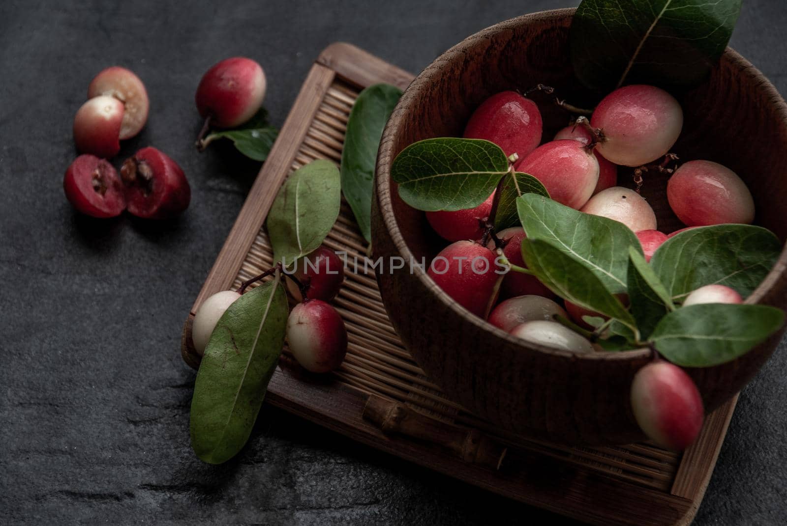 Bengal-Currants, Carandas-plum or Karonda fruit (Carissa carandas L.) sour taste fruit in Wooden cup on wicker. Oblique view from the top.