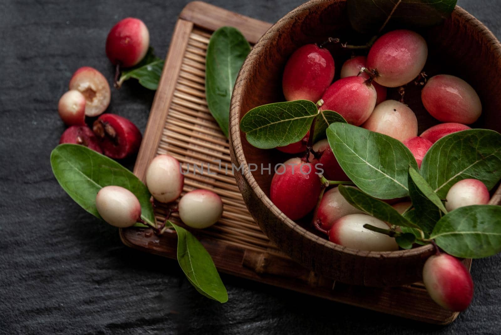 Bengal-Currants, Carandas-plum or Karonda fruit (Carissa carandas L.) sour taste fruit in Wooden cup on wicker. Oblique view from the top.
