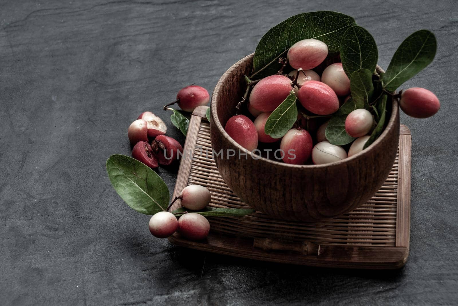 Bengal-Currants, Carandas-plum or Karonda fruit (Carissa carandas L.) sour taste fruit in Wooden cup on wicker. Oblique view from the top.