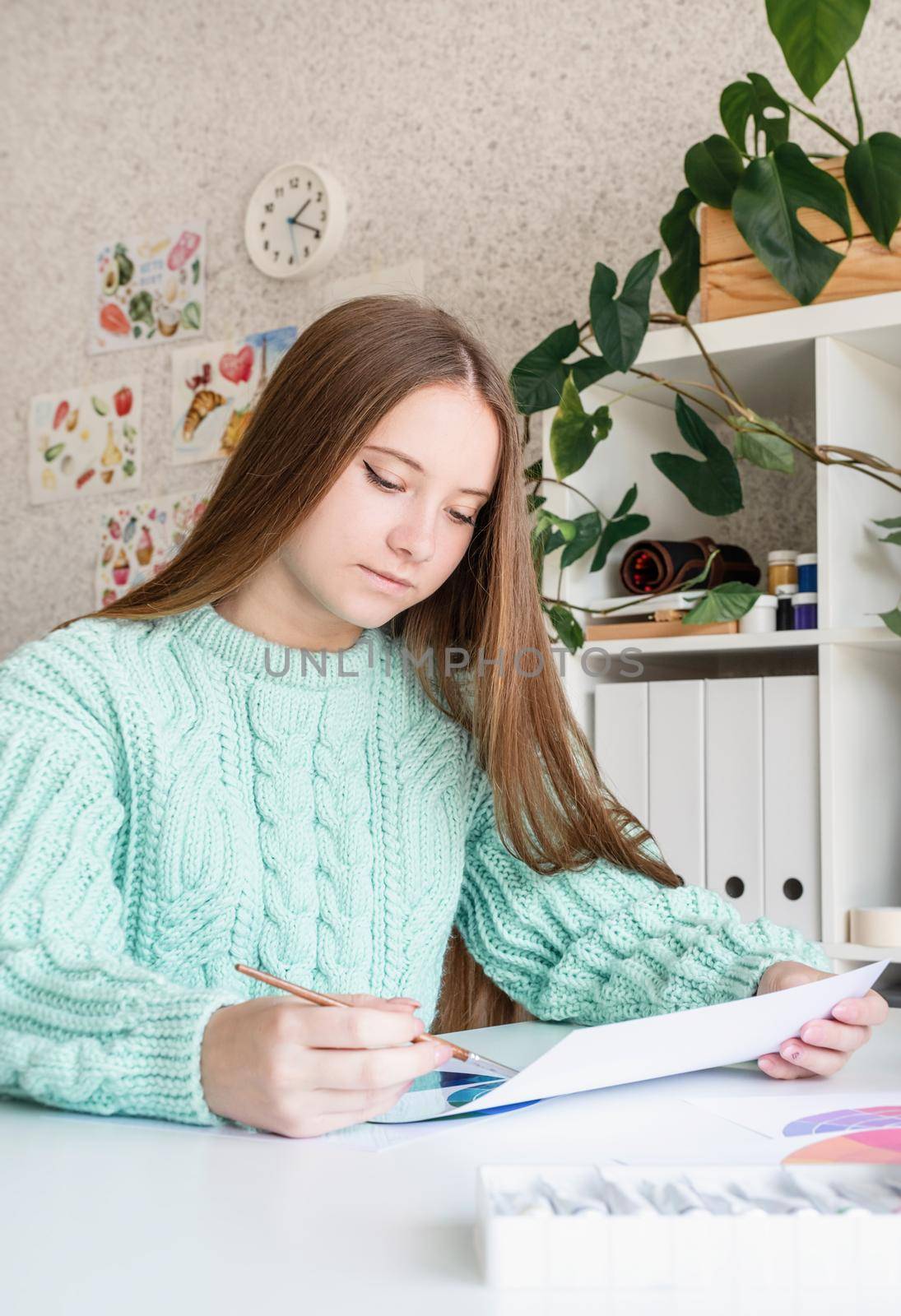 Young smiling woman artist holding color palette working in her studio by Desperada