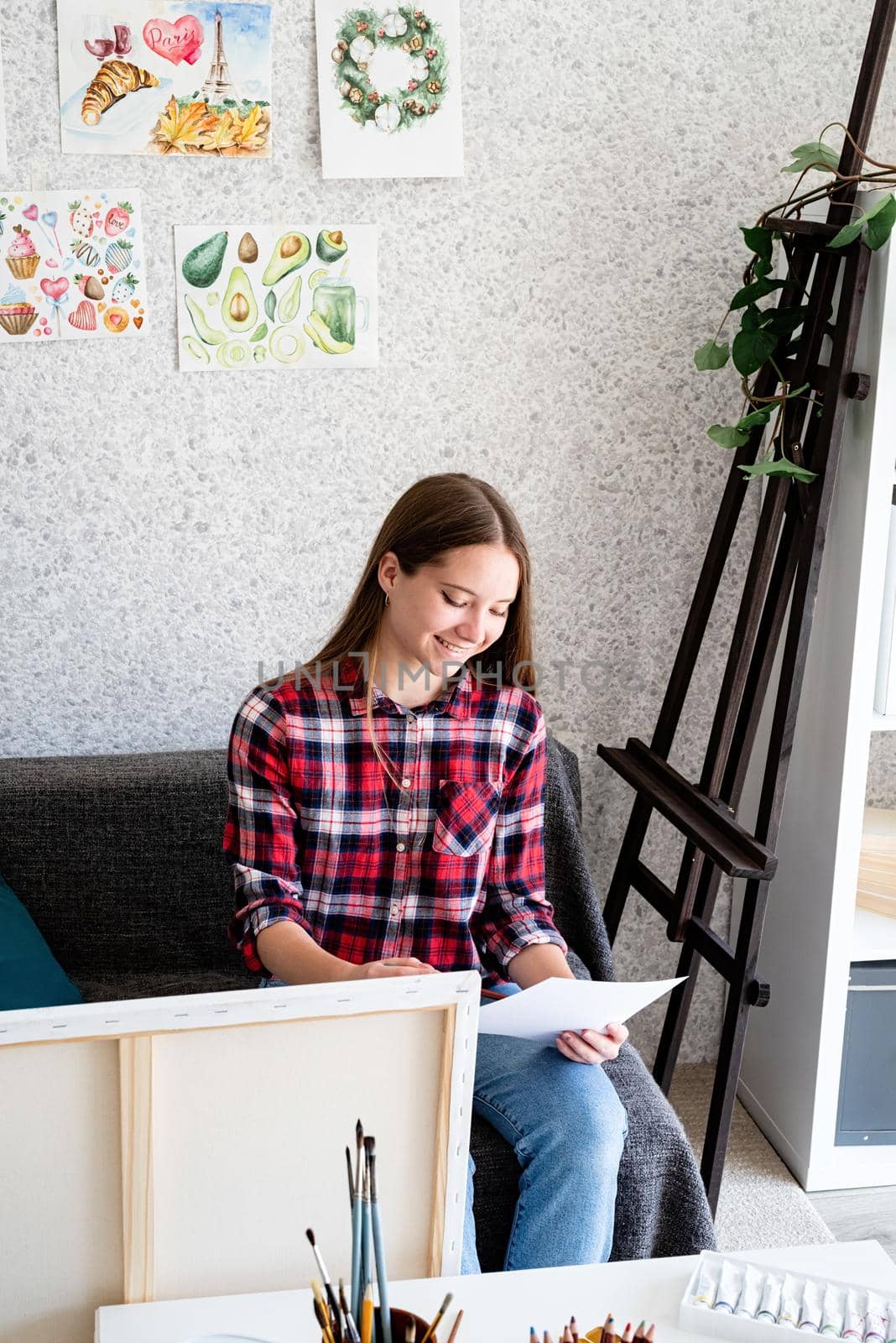 Young woman artist in check shirt painting a picture at home