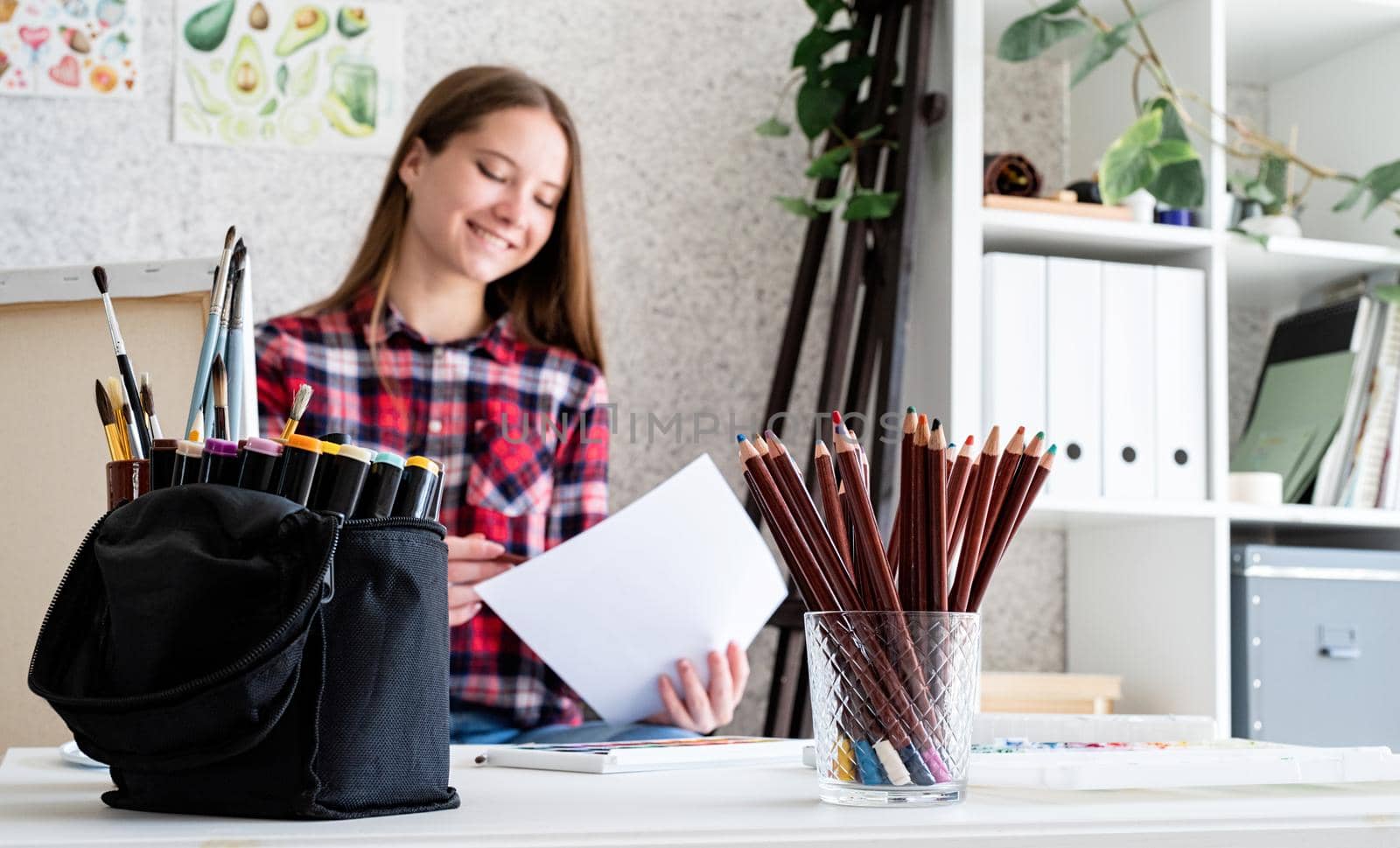 Young woman artist in check shirt painting a picture at home. Focus on foreground