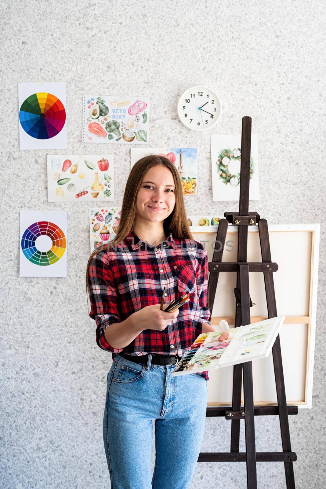 Young woman artist in check shirt painting a picture at home