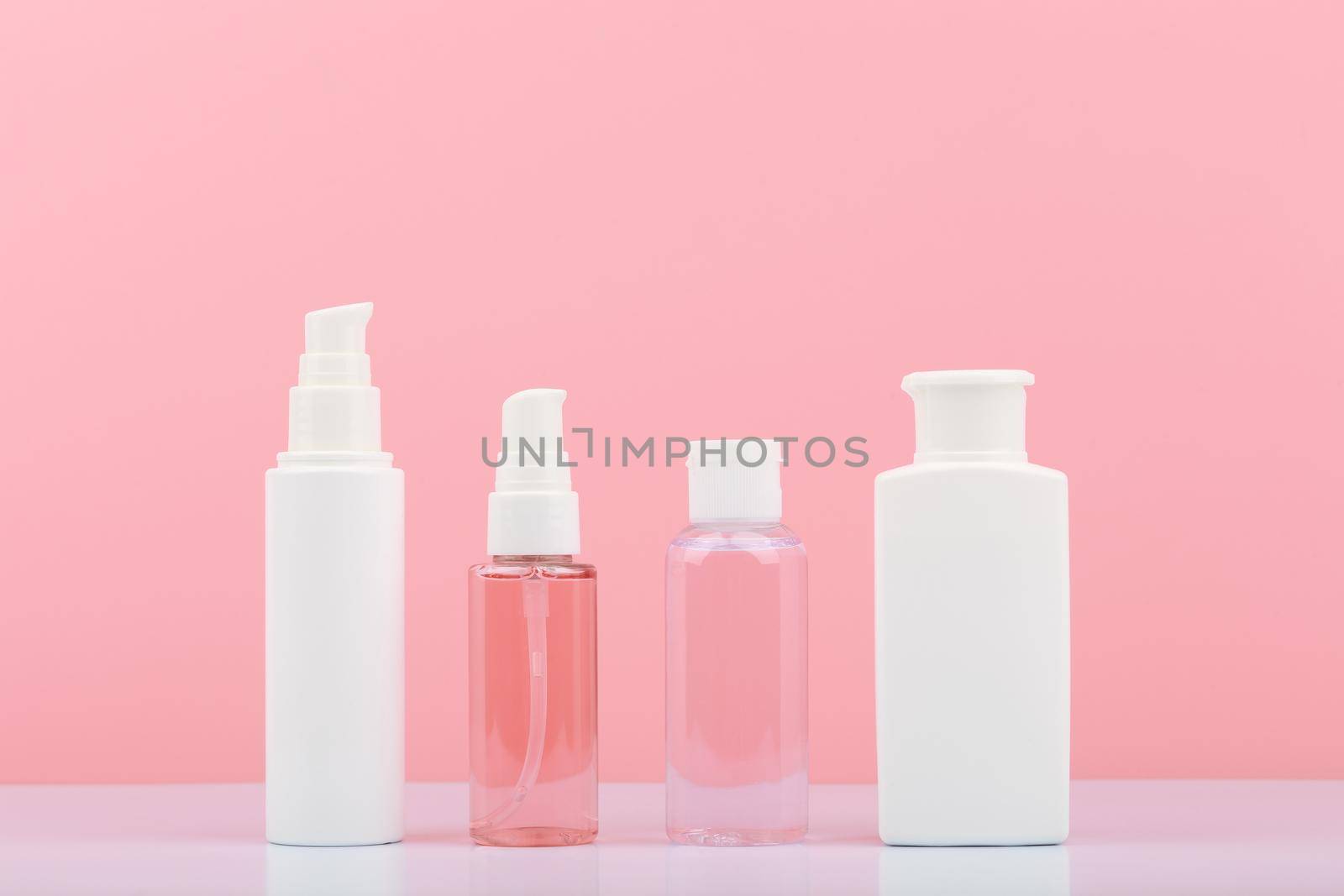 Set of cosmetic products for skin cleaning, exfoliating and moisturizing. Cosmetic bottles against pink background. Concept of skin care and beauty