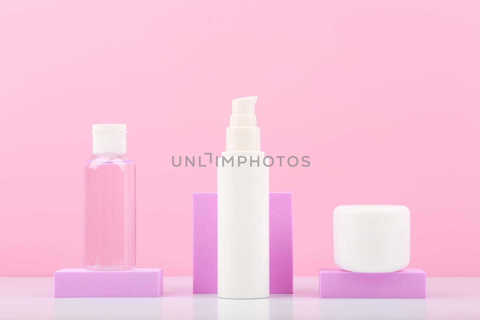 Cosmetic set with lotion, face cream and under eye cream on podiums against bright pink background. Concept of daily skin care routine or anti aging skin treatment