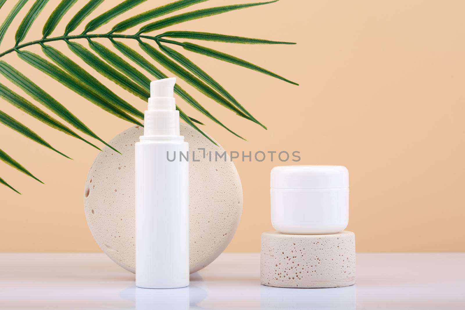 Face cream and under eye cream against beige background with palm leaf. Beauty products for woman. Daily skin care routine concept