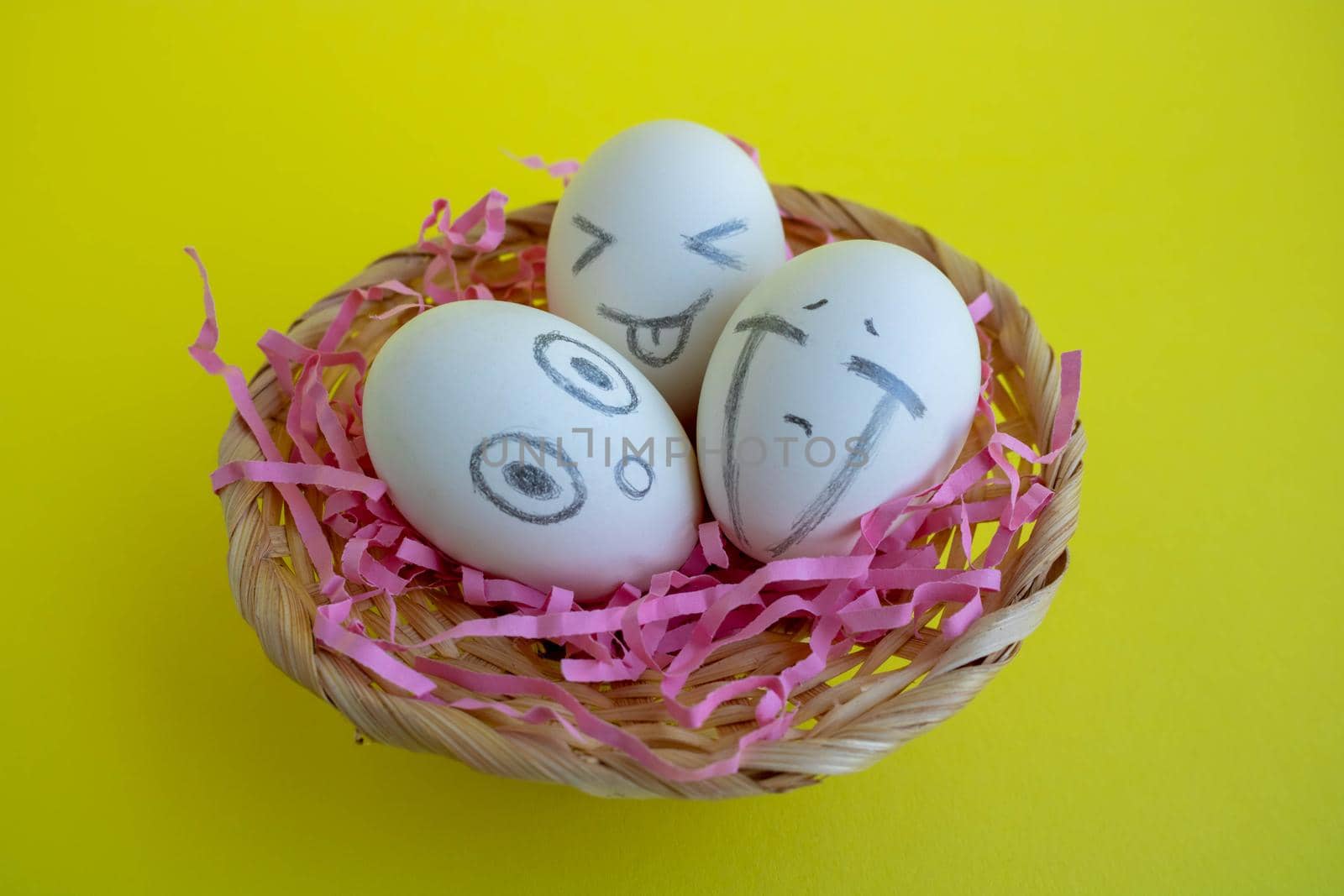 In the basket are three charming white eggs with faces on a yellow background. Easter Concept.