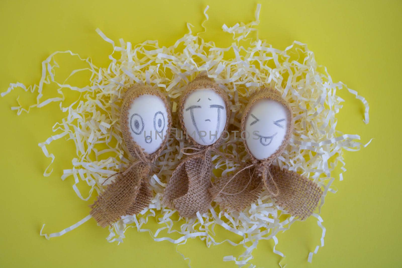 White eggs with funny faces in sackcloth on a yellow background. Easter Concept.