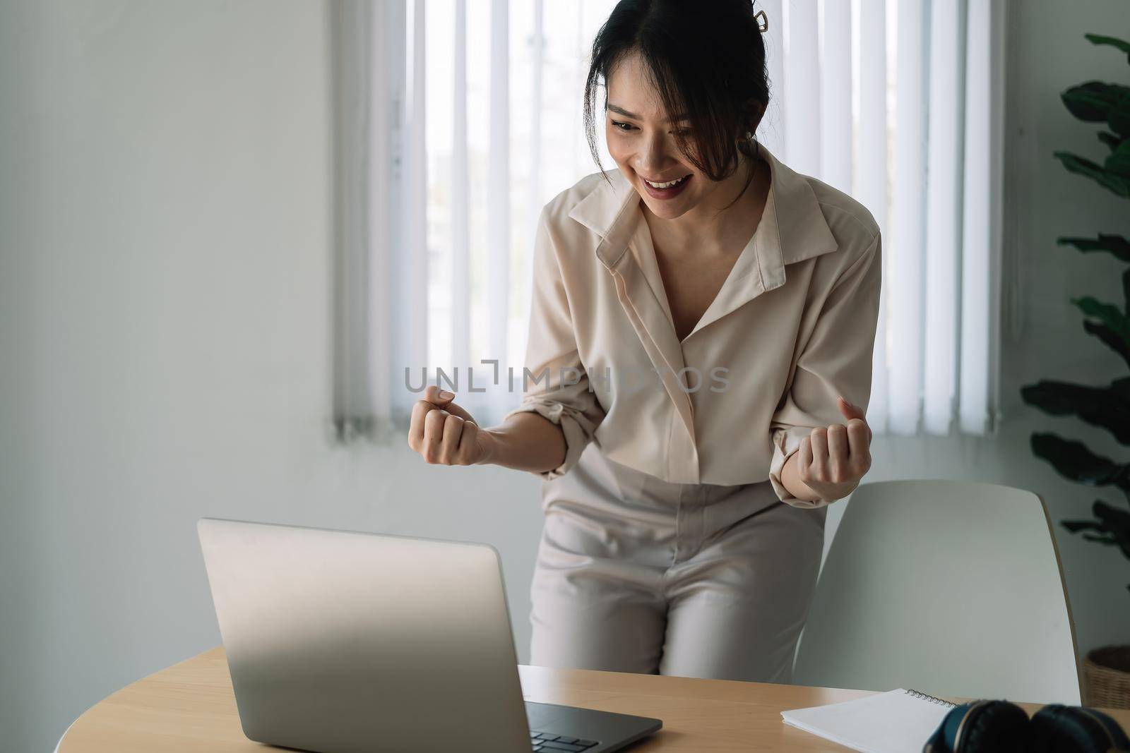 Excited Asian Businesswoman Celebrating Success At Workplace. by nateemee