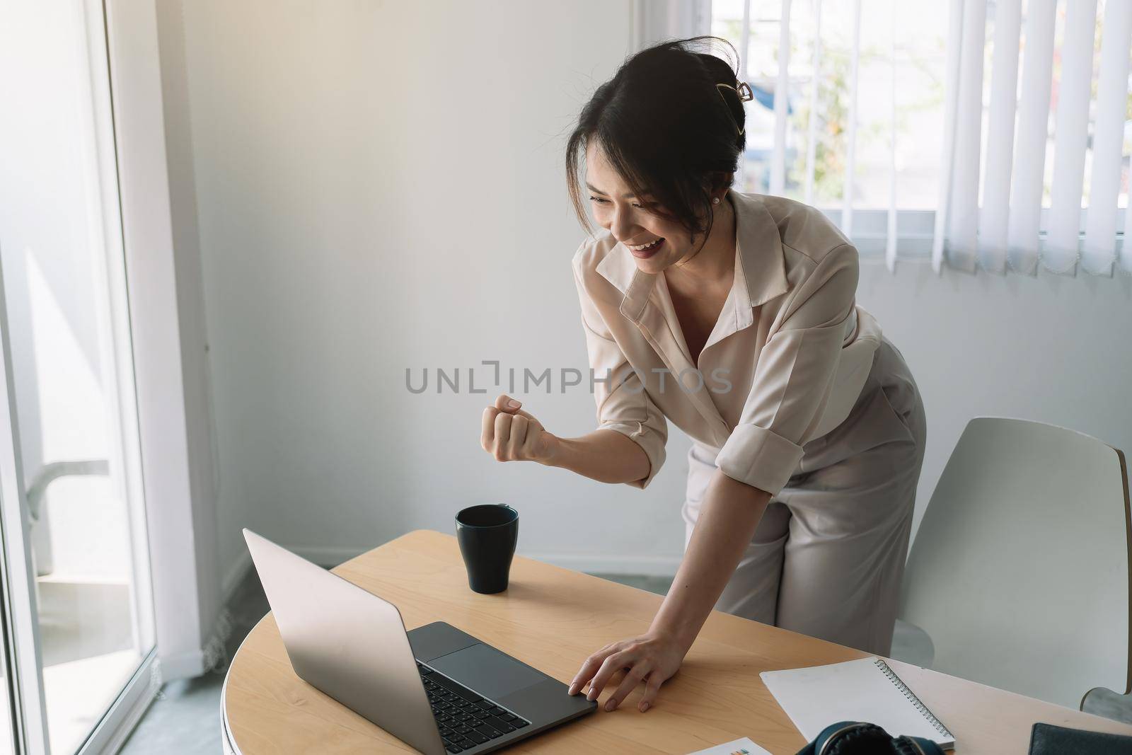 Excited Asian Businesswoman Celebrating Success At Workplace. by nateemee