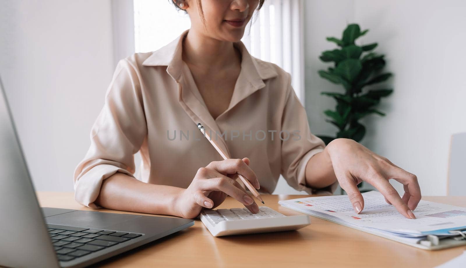 Close up of businesswoman or accountant hand holding pencil working on calculator to calculate financial data report, accountancy document and laptop computer at office, business concept. by nateemee