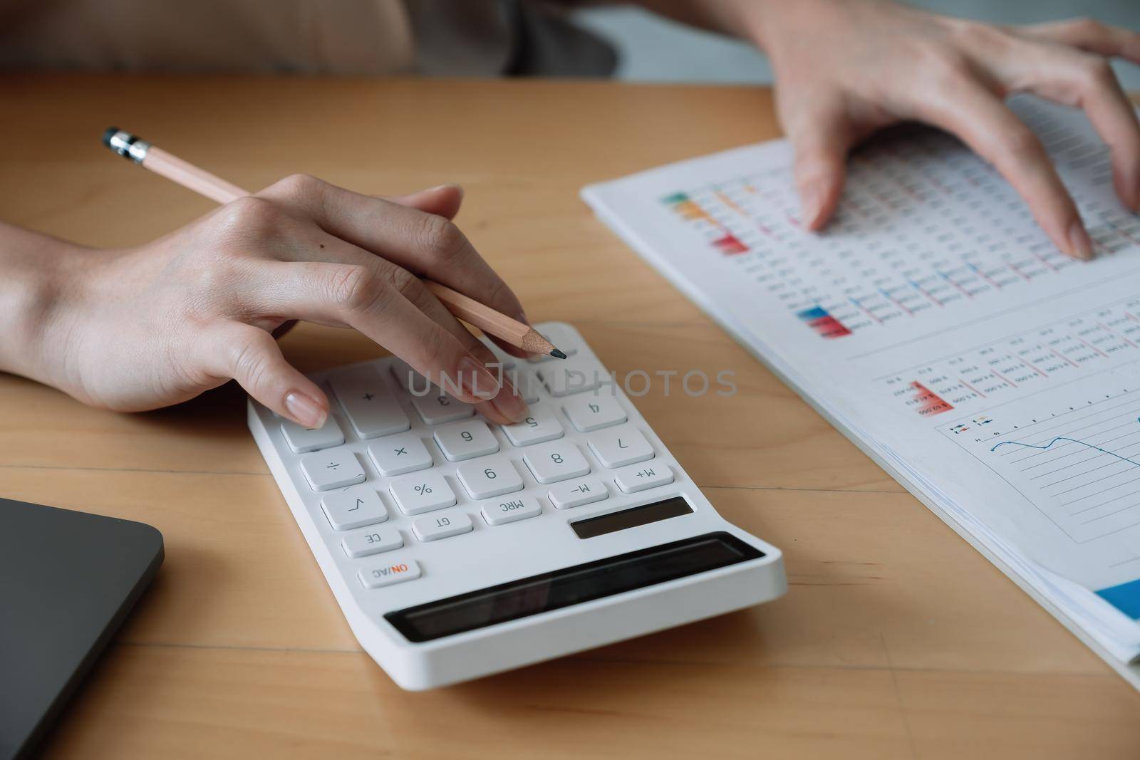 Close up of businesswoman or accountant hand holding pencil working on calculator to calculate financial data report, accountancy document and laptop computer at office, business concept by nateemee