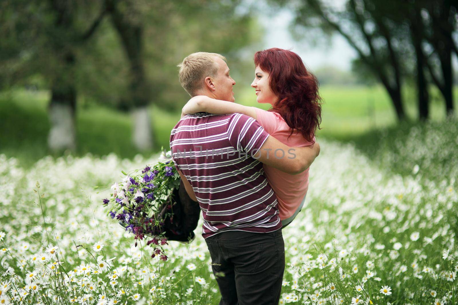 The guy holds the girl in his arms in a green park with white daisies by selinsmo