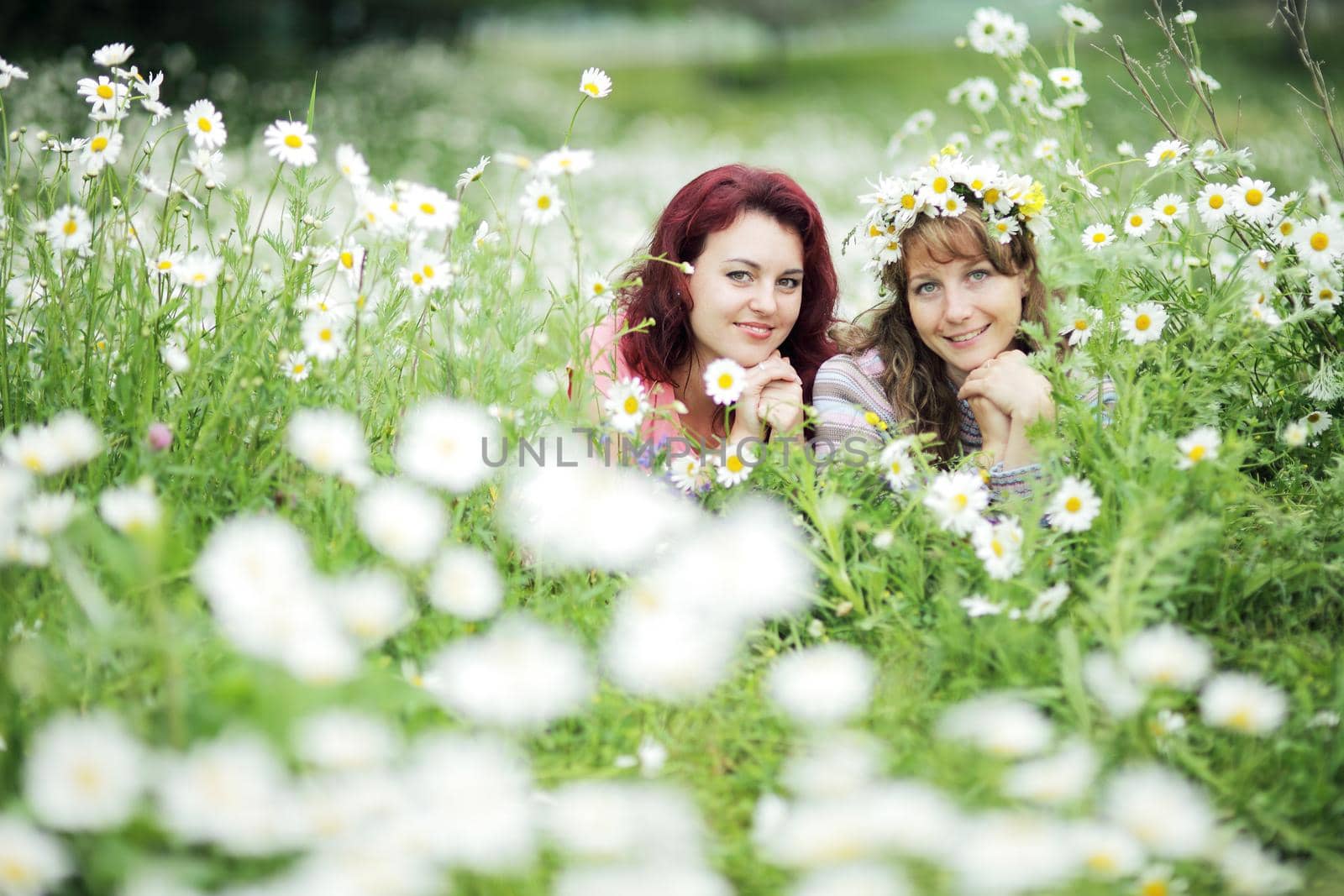 Two girls lie on a green meadow with white daisies by selinsmo