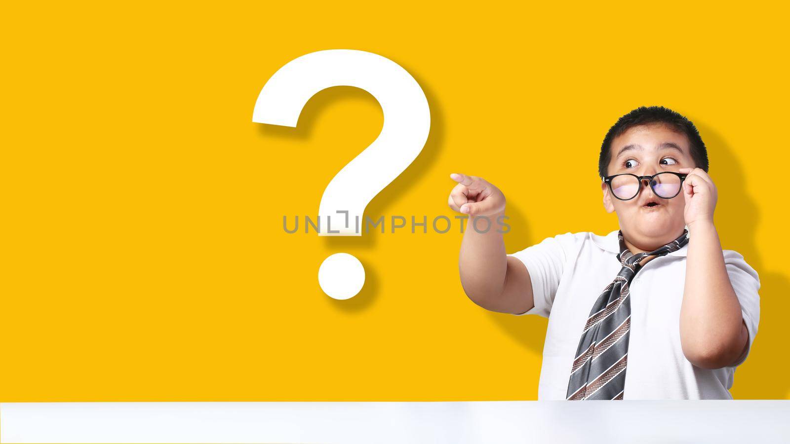 Asian boy pointing to big question mark on yellow background