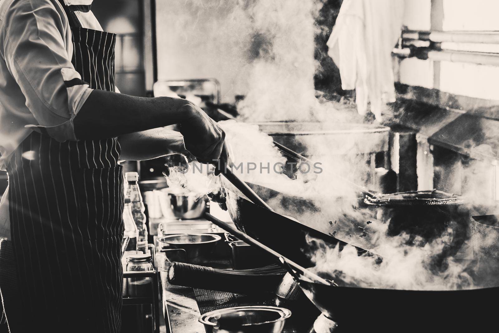 Chef stir fry in wok. Dramatic cooking with fire hard in kitchen, Black and white filter
