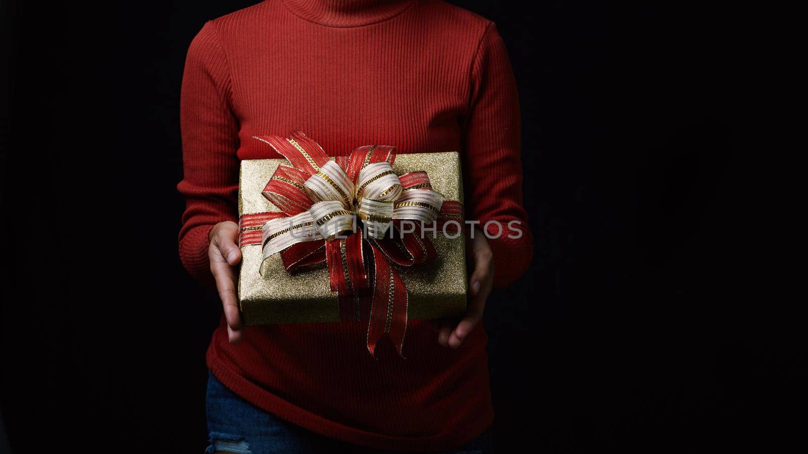 Young woman hands holding gold gift box on dark background