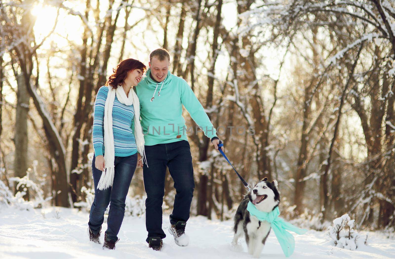 Young couple smiling and having fun in winter park with their husky dog.