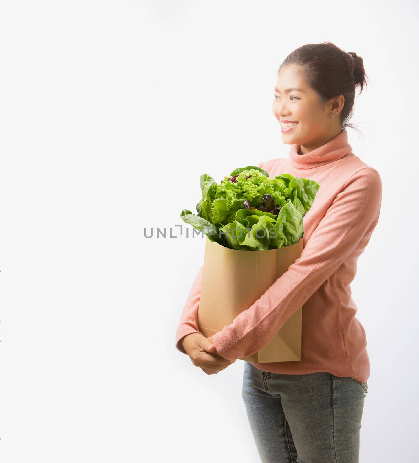 Asian woman holding paper shopping bag full of green vegetables on white background