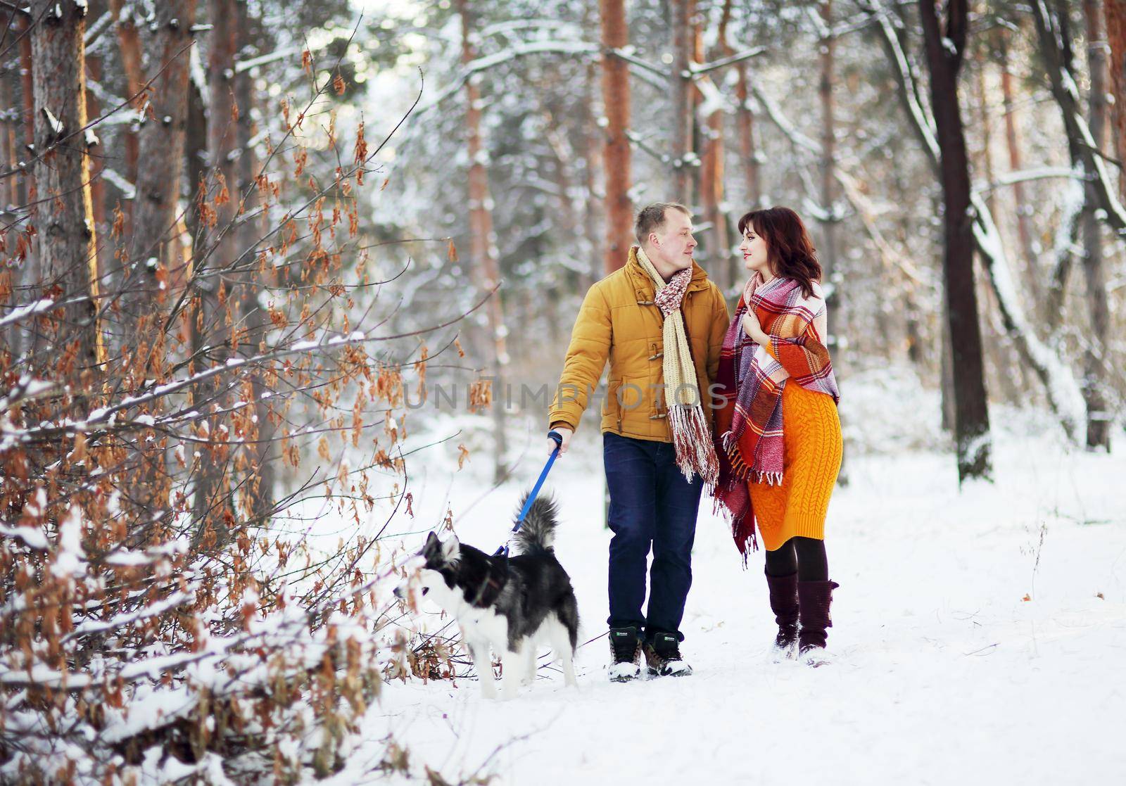 Young couple smiling and having fun in winter park with their husky dog.