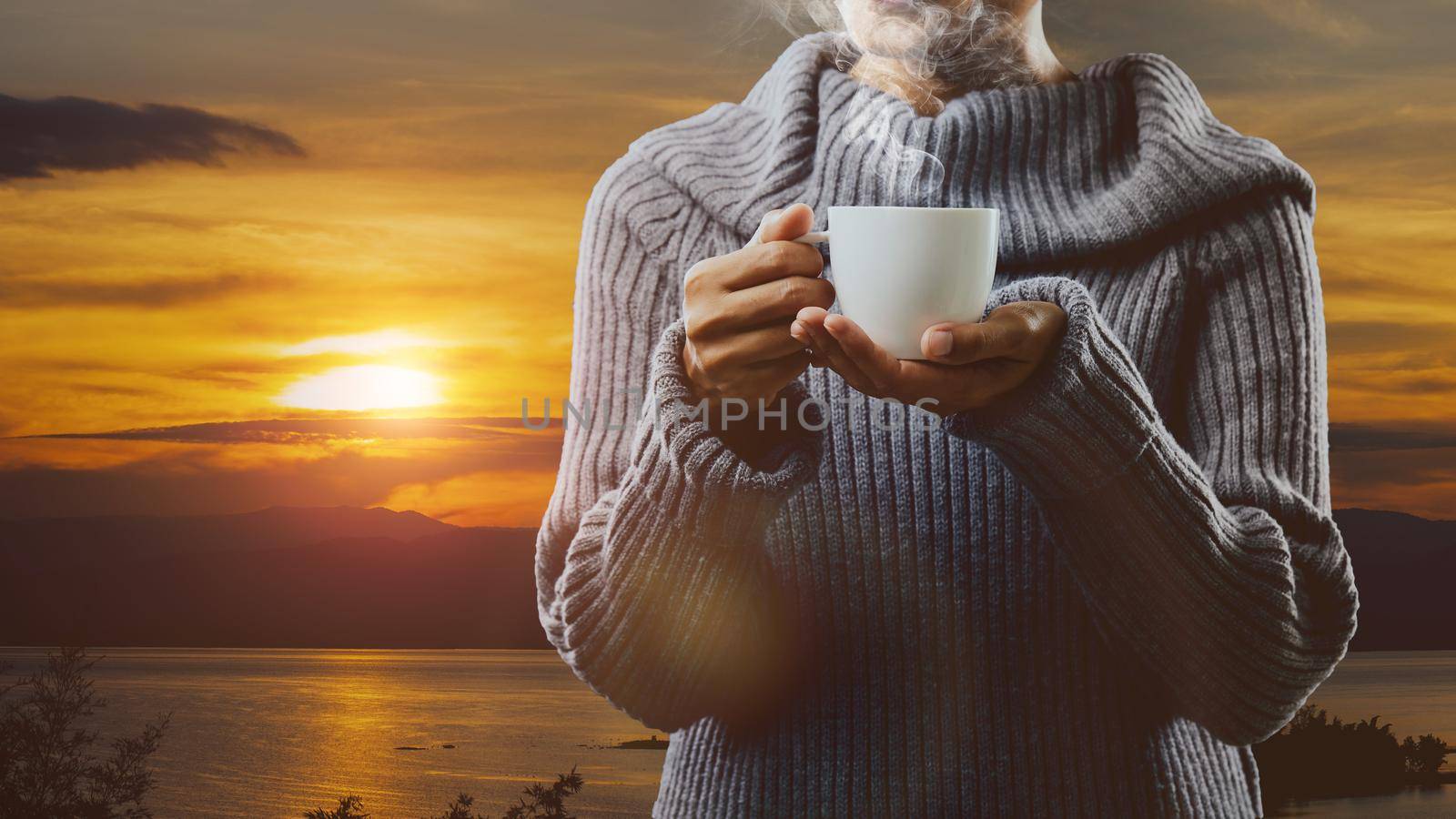 Holding white cup of coffee with sunrise