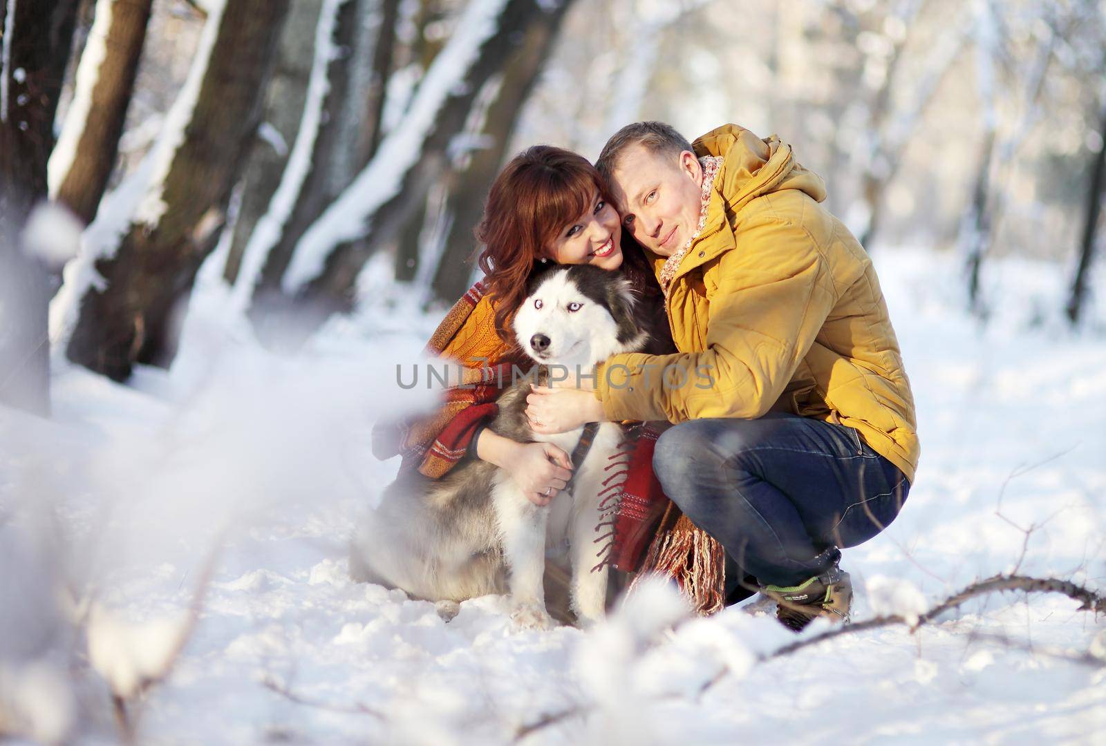 Couple smiling and having fun in winter park with their siberian husky dog.