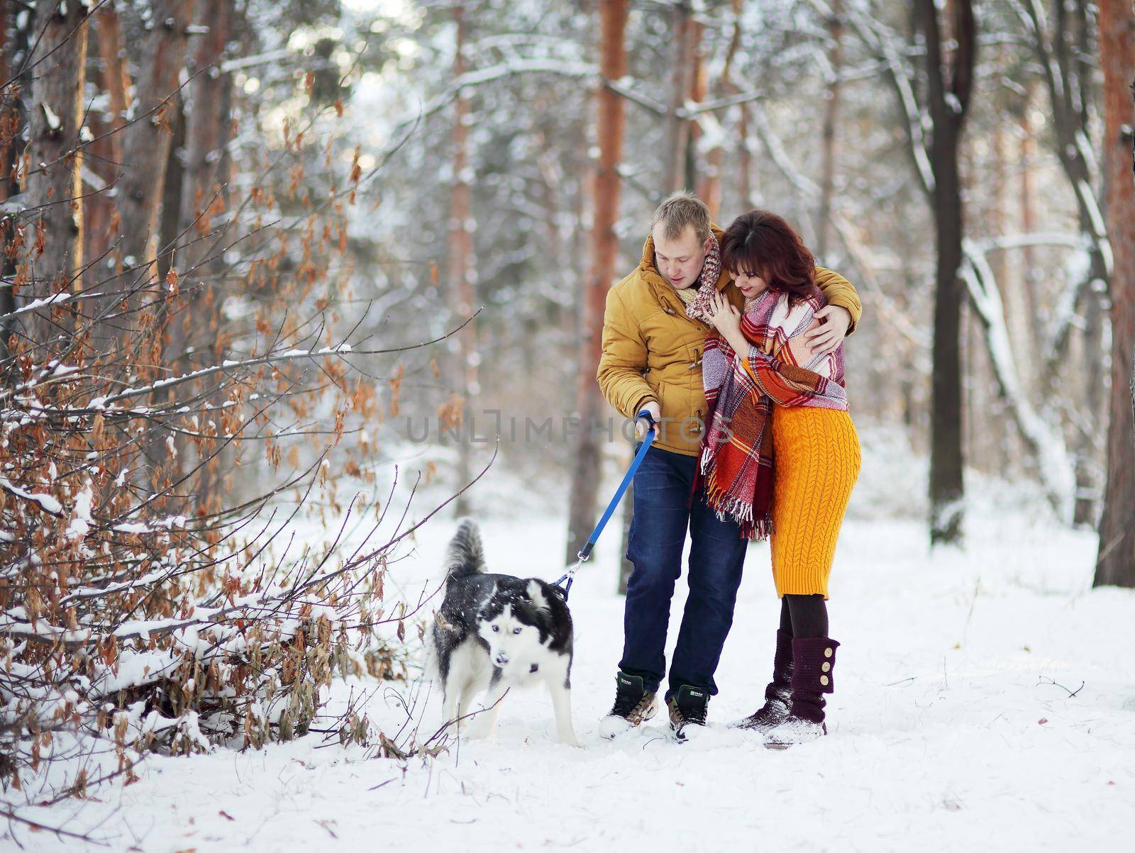 Young couple smiling and having fun in winter park with their husky dog.
