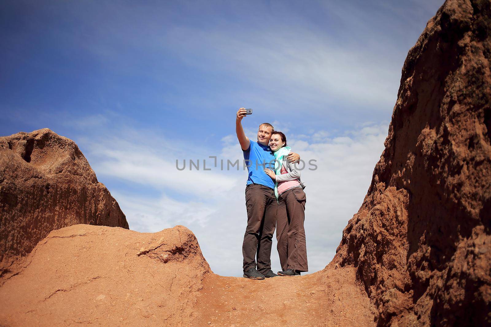 A guy and a girl take a selfie while on the top of the mountain against the background of the sky.