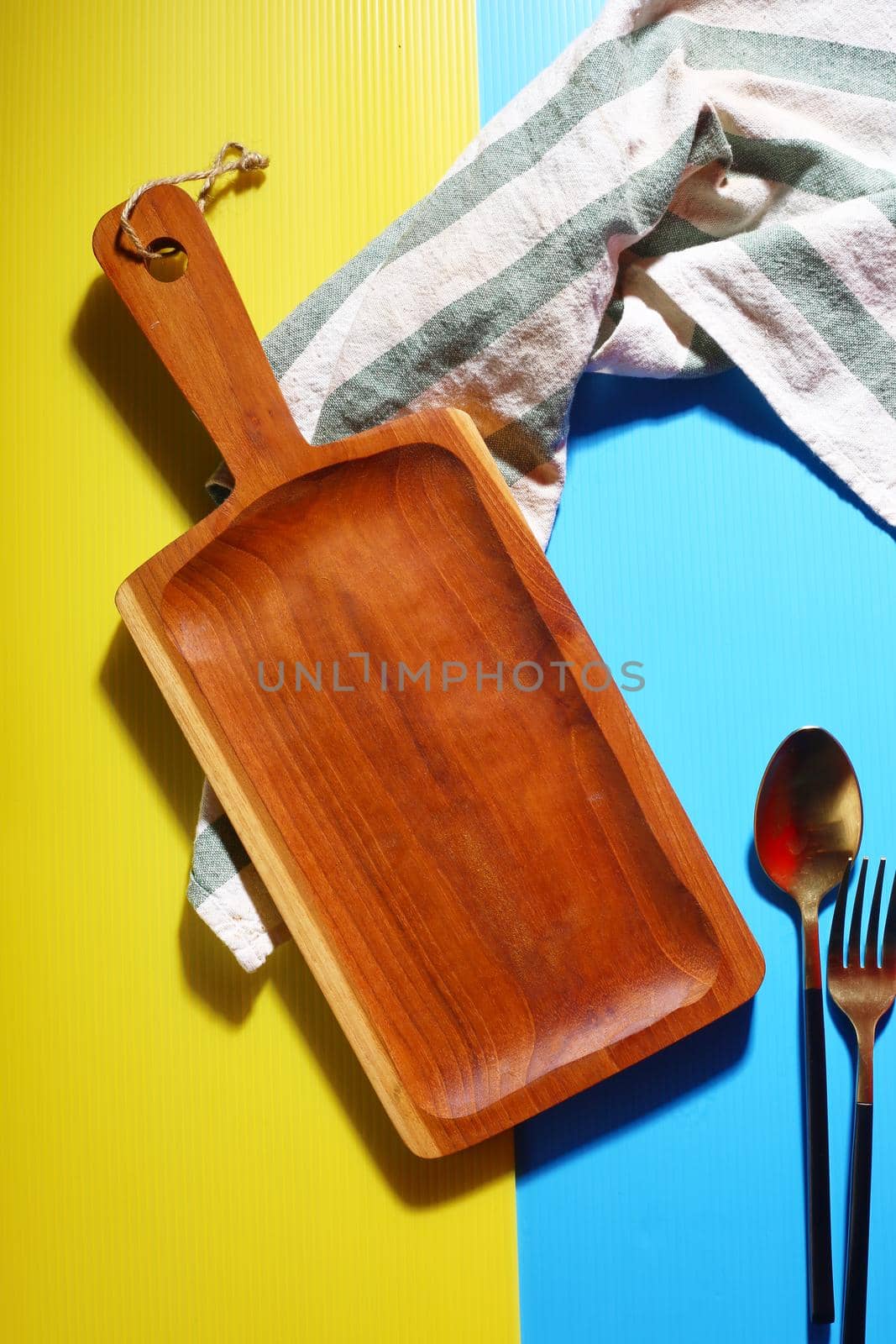 Empty wooden tray placed with spoon on a colorful background
