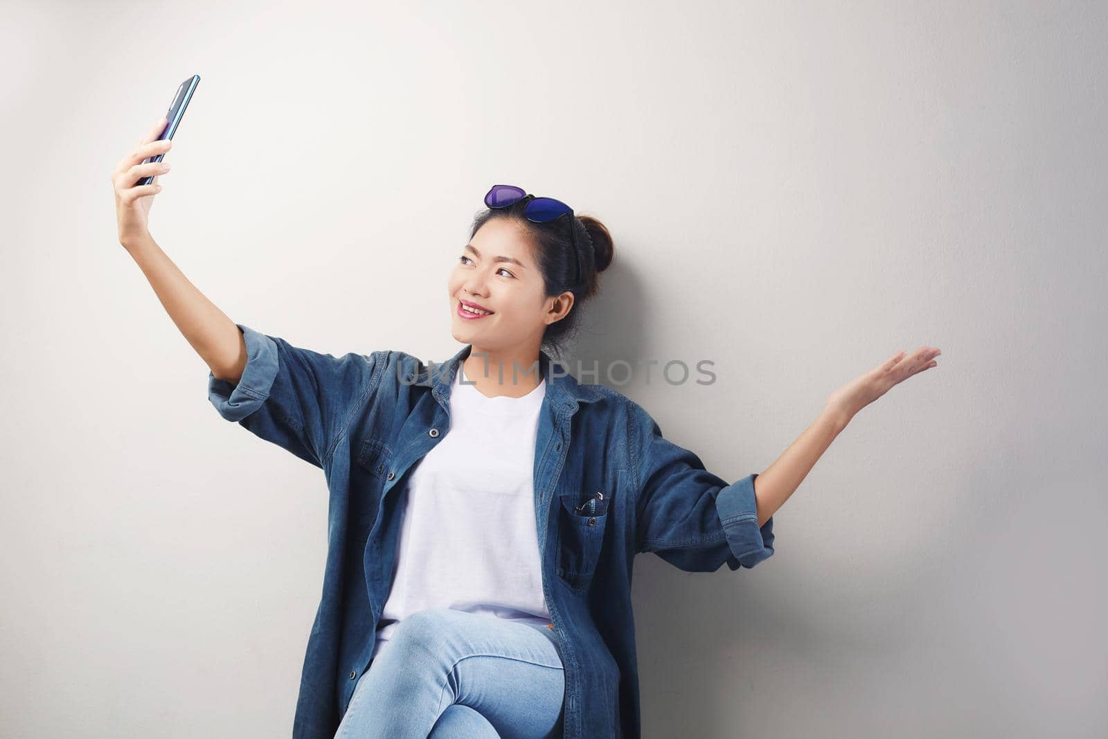 Smiling young Asian woman making video call on smartphone over gray background