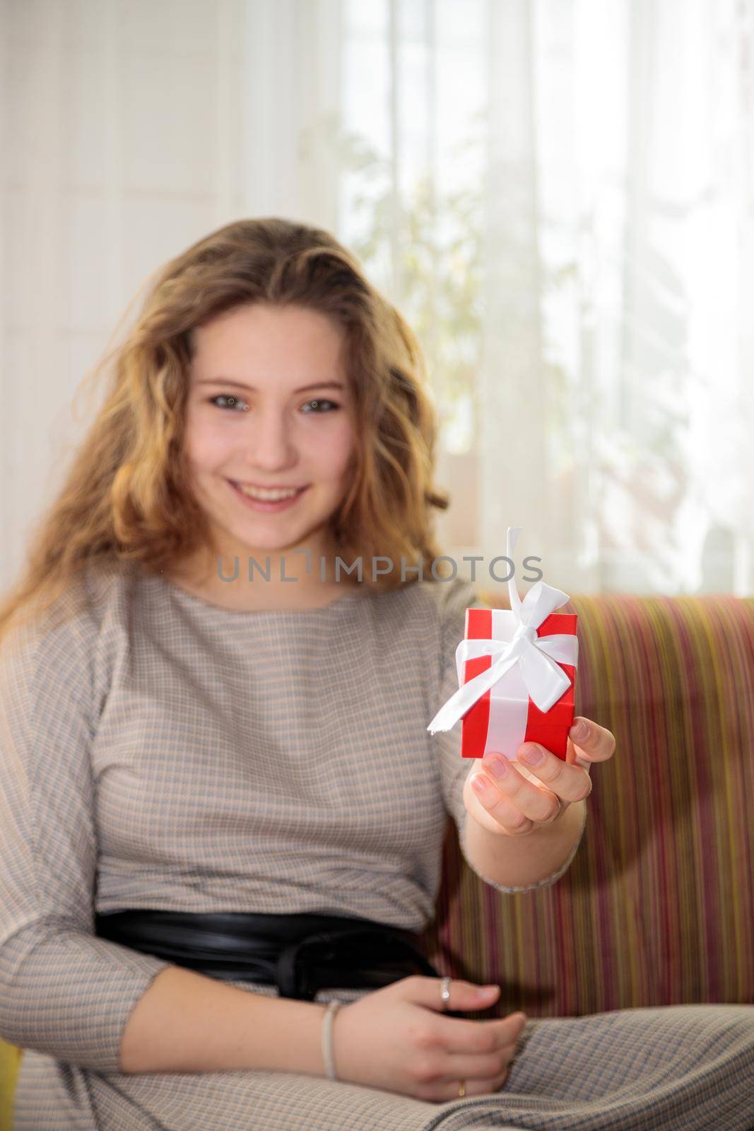 A young girl with long hair is tying a gift box for congratulations. Sits on the couch in the room