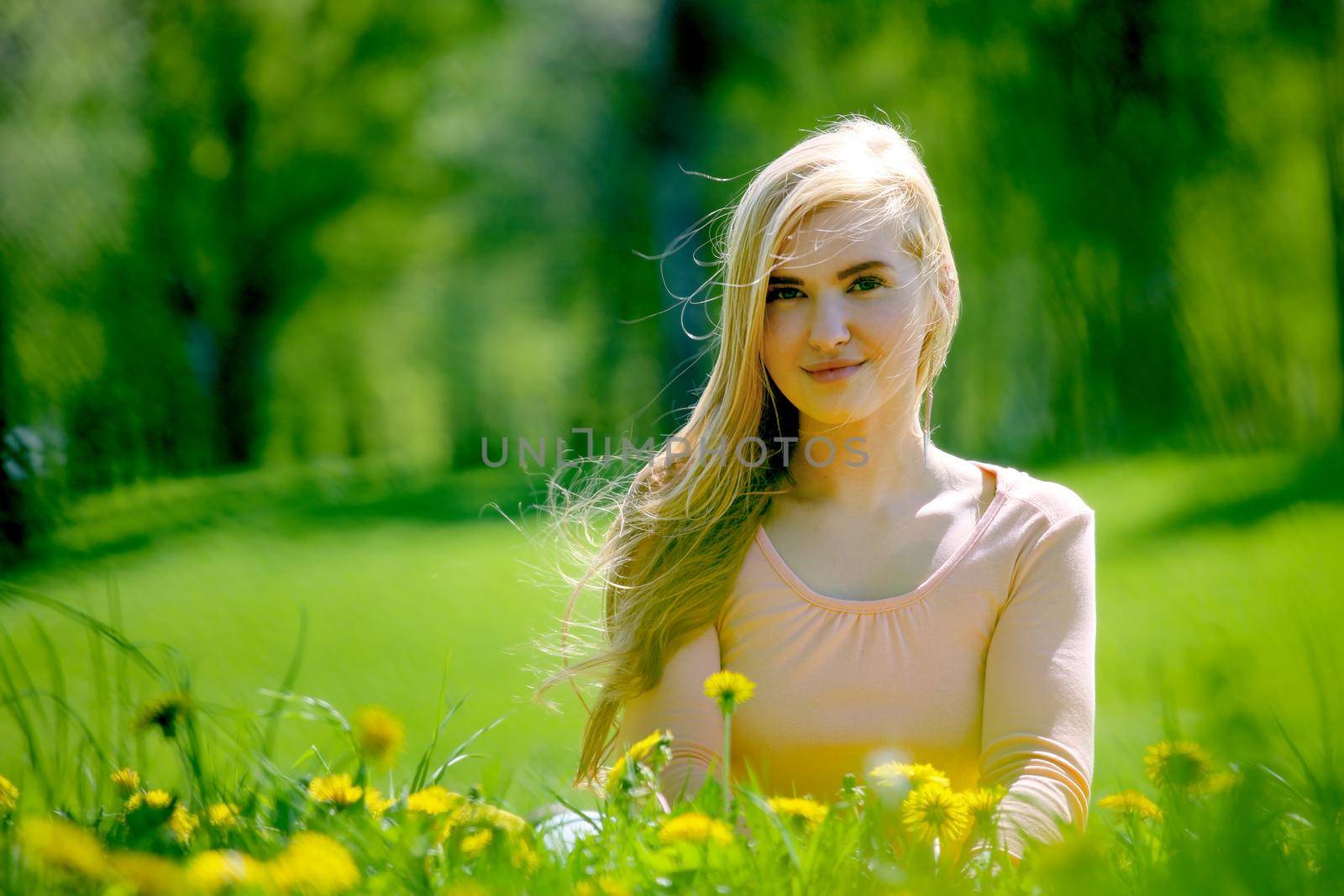 Beautiful young woman laying in spring park with dandelion flowers