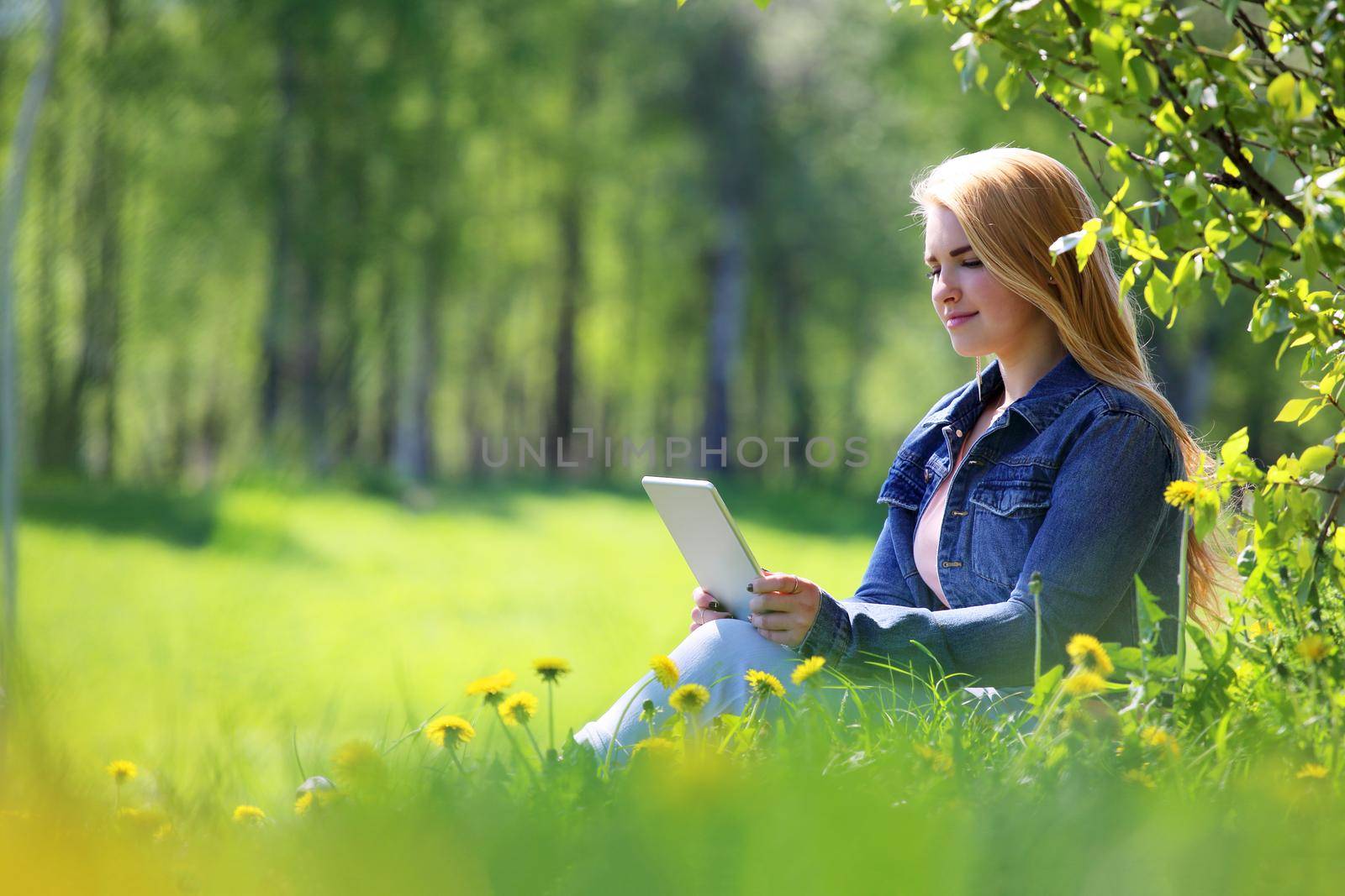 Young woman using tablet in spring park with flowers