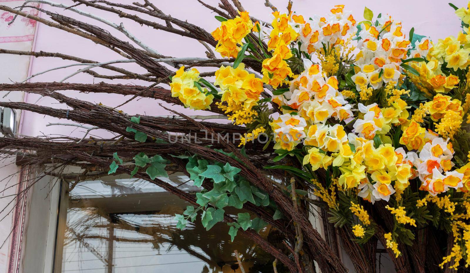 The shop is decorated with bright, artificial flowers, daffodils and branches. A fragment of a building decorated with flowers.