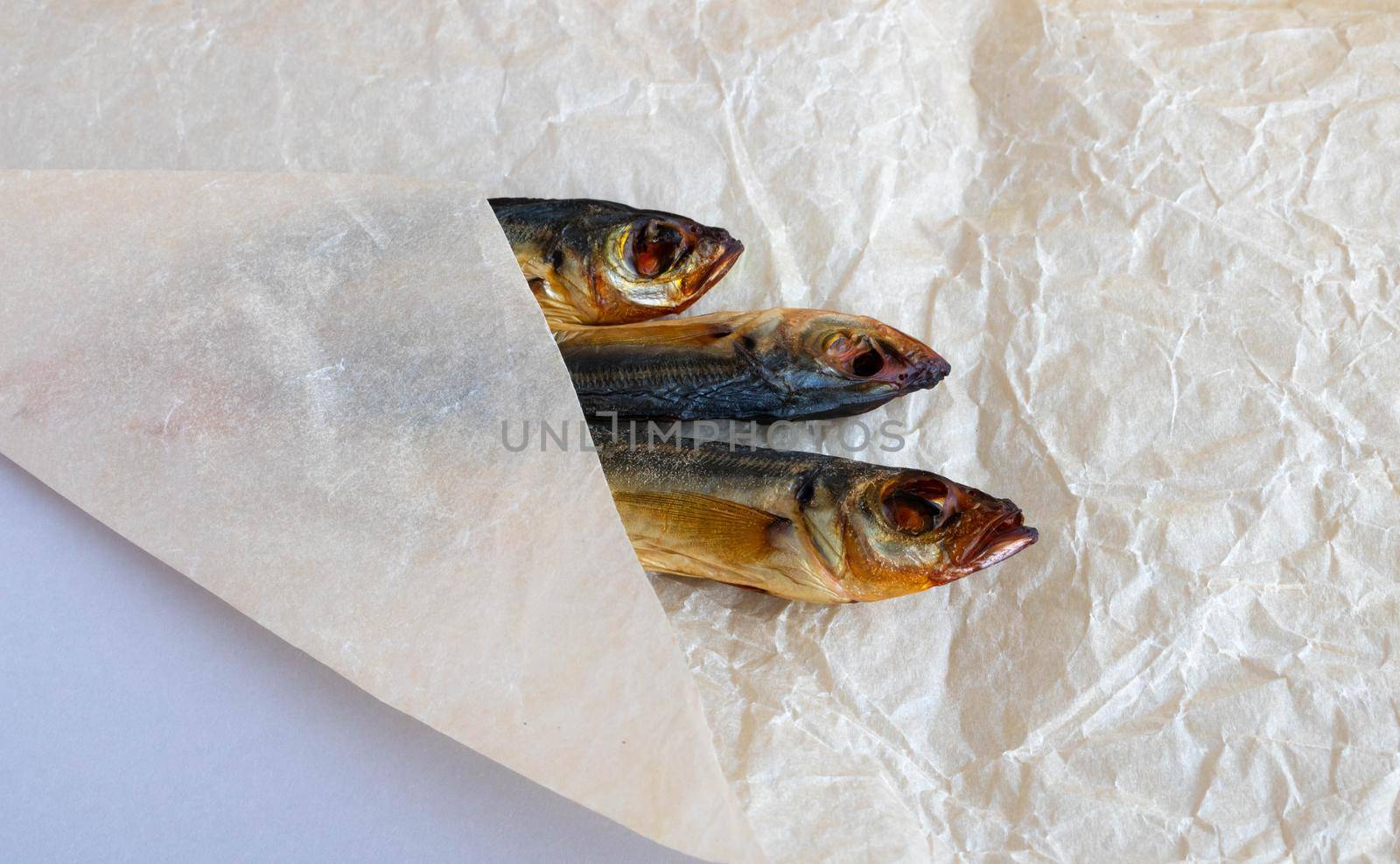 A smoked horse mackerel close-up lies wrapped on a crumpled paper background .