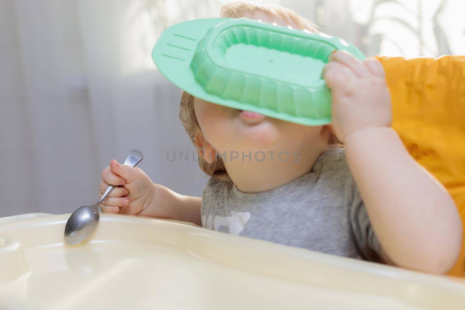 Little child sits on a high chair and eats with a spoon. Close-up