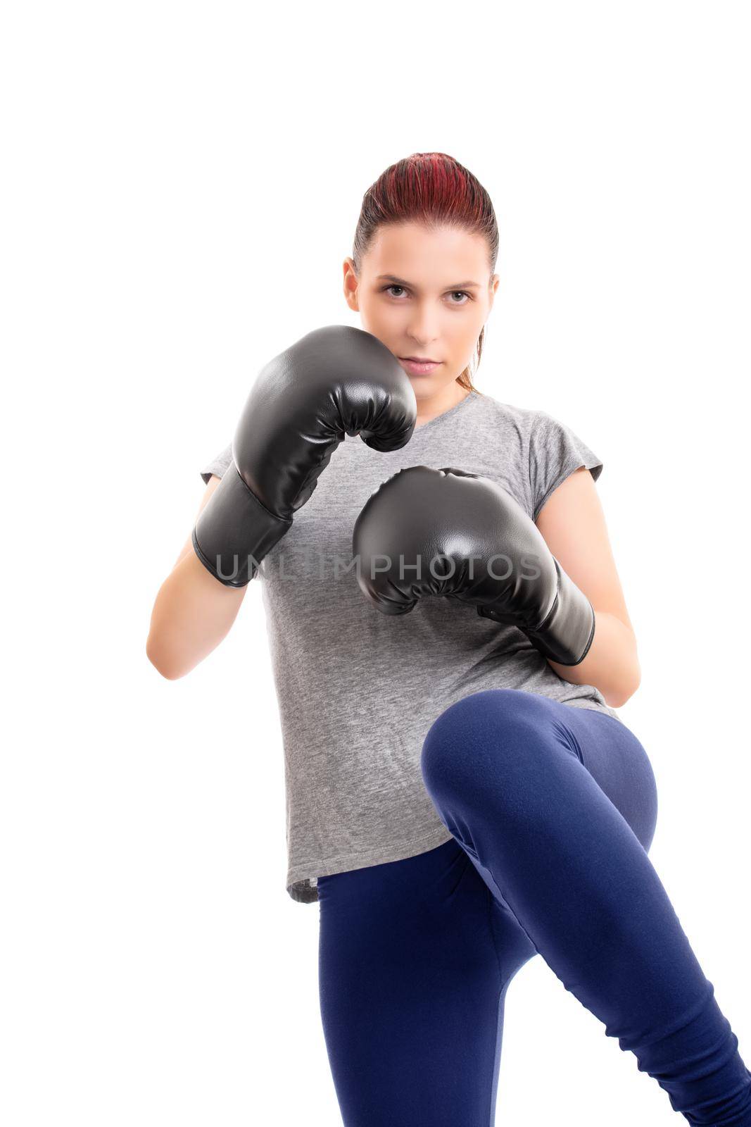 Portrait of a beautiful young serious girl with boxing gloves lifting her knee, isolated on white background. Combat sport concept.
