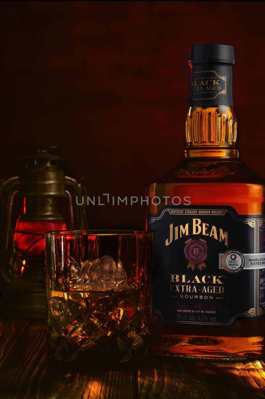Bottle of Jim Beam Black Extra Aged Bourbon whiskey and glass with drink and ice on Red background. by Fischeron