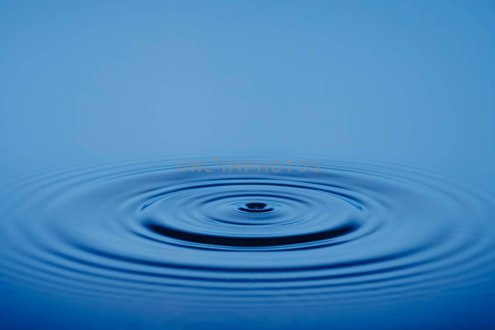 Closeup Water drop or splash falling on the surface of the water and beautiful circular wave ripple, water concept, with blue background