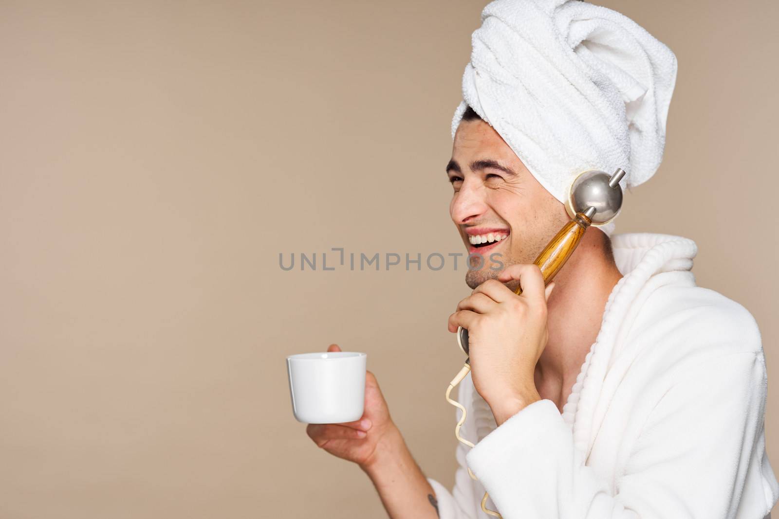 Happy man talking on the phone with a cup of coffee and a towel on his head.