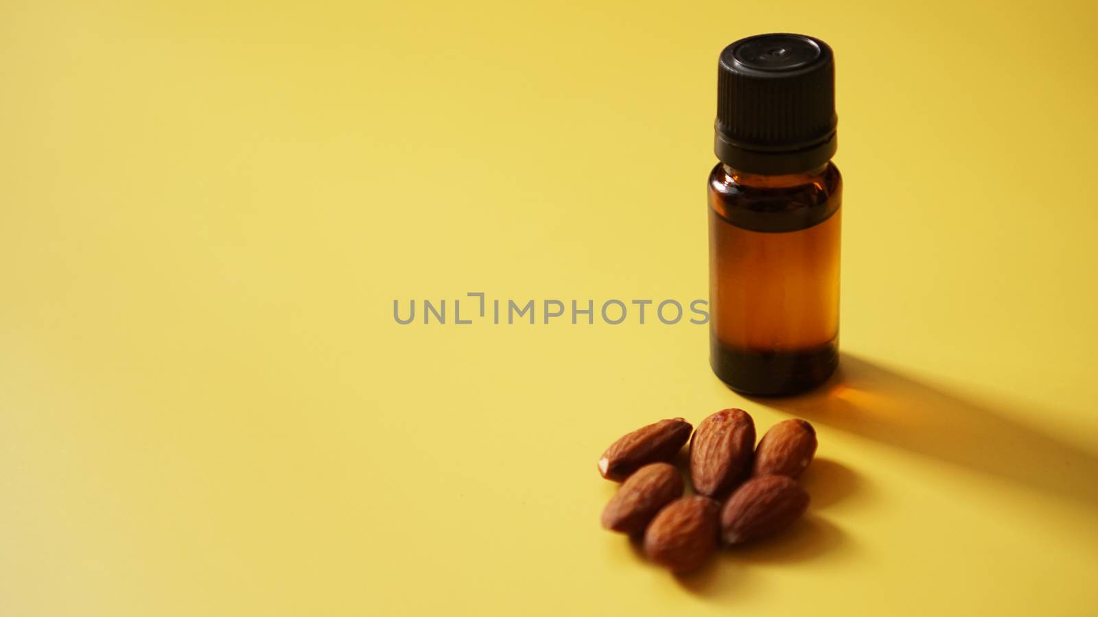 Bottle of almond oil and almonds on yellow background by natali_brill