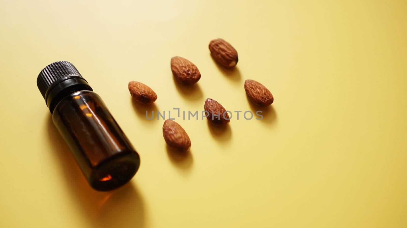 Bottle of almond oil and almonds on yellow background - Bottle and rows of nuts