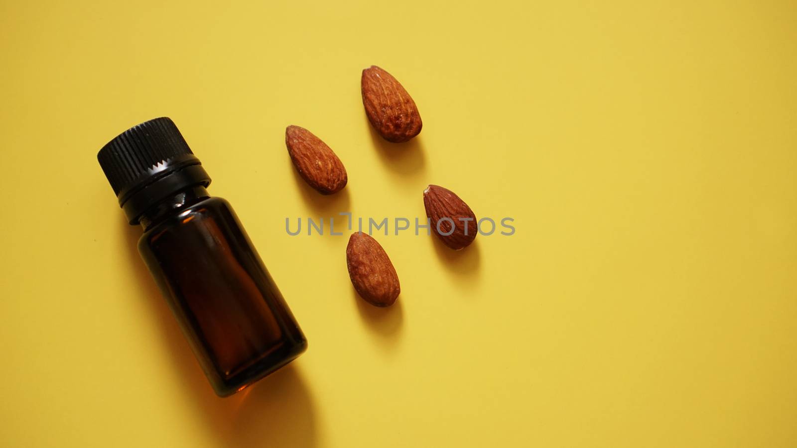 Bottle of almond oil and almonds on yellow background - Bottle and rows of nuts