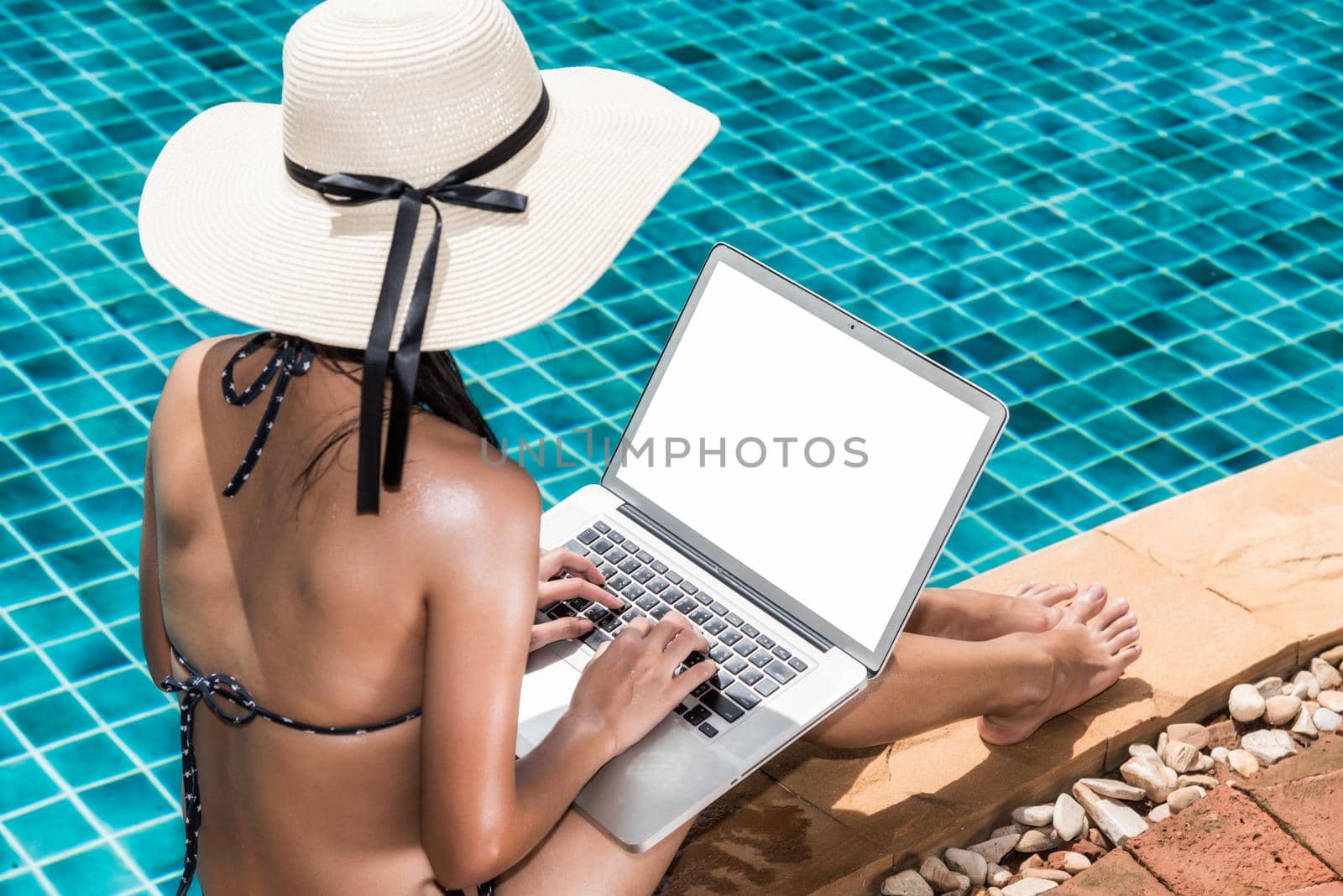 Asian Woman working on laptop computer sitting at poolside blue water