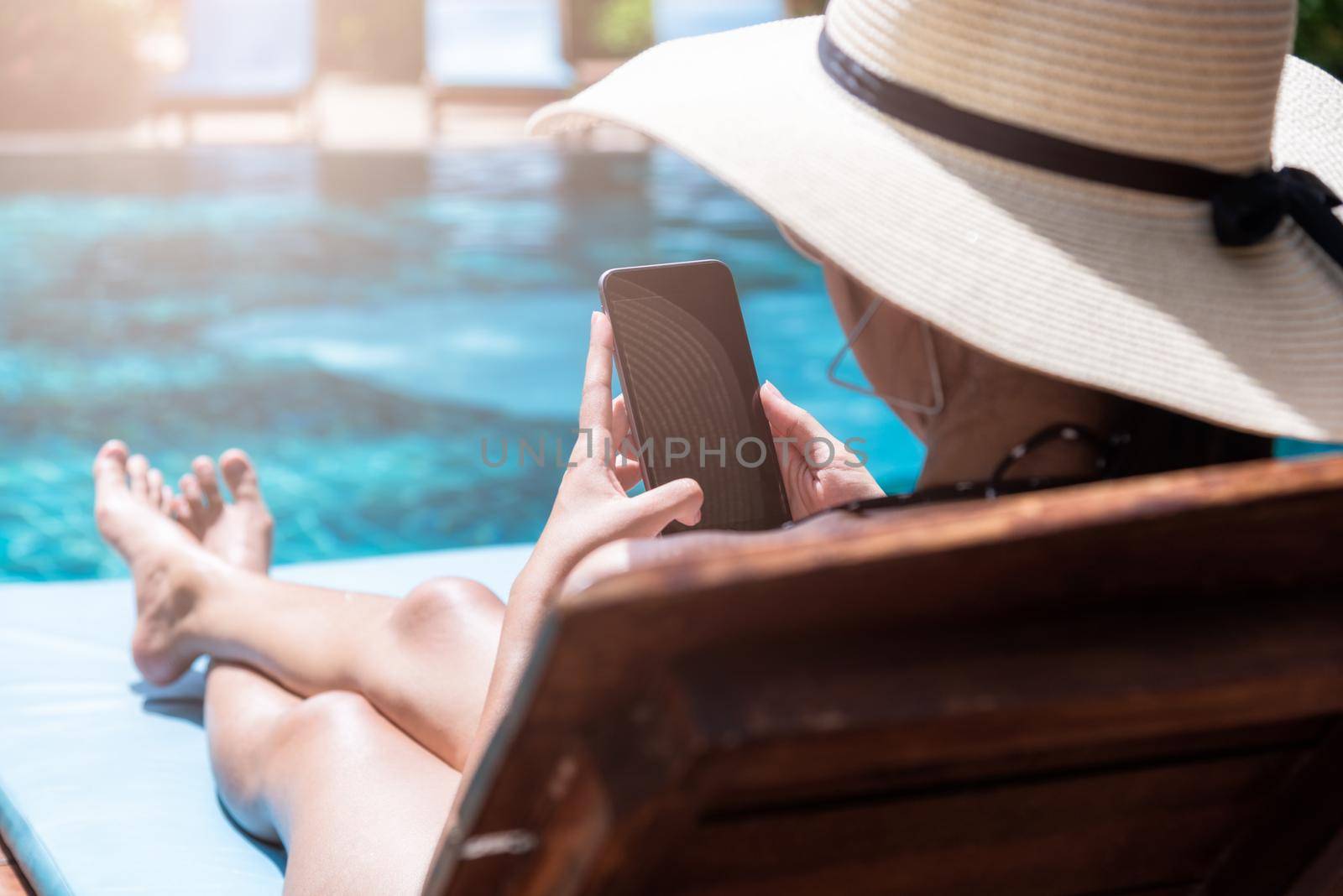 Beautiful girl woman with big hat happy use smartphone relaxing near swimming pool blue water