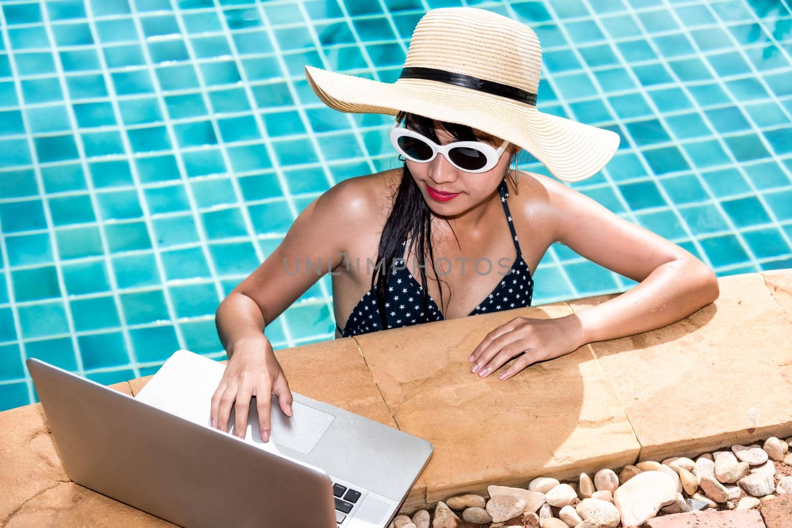 Beautiful girl woman in bikini relaxing pool and using laptop on edge while smiling, blue water