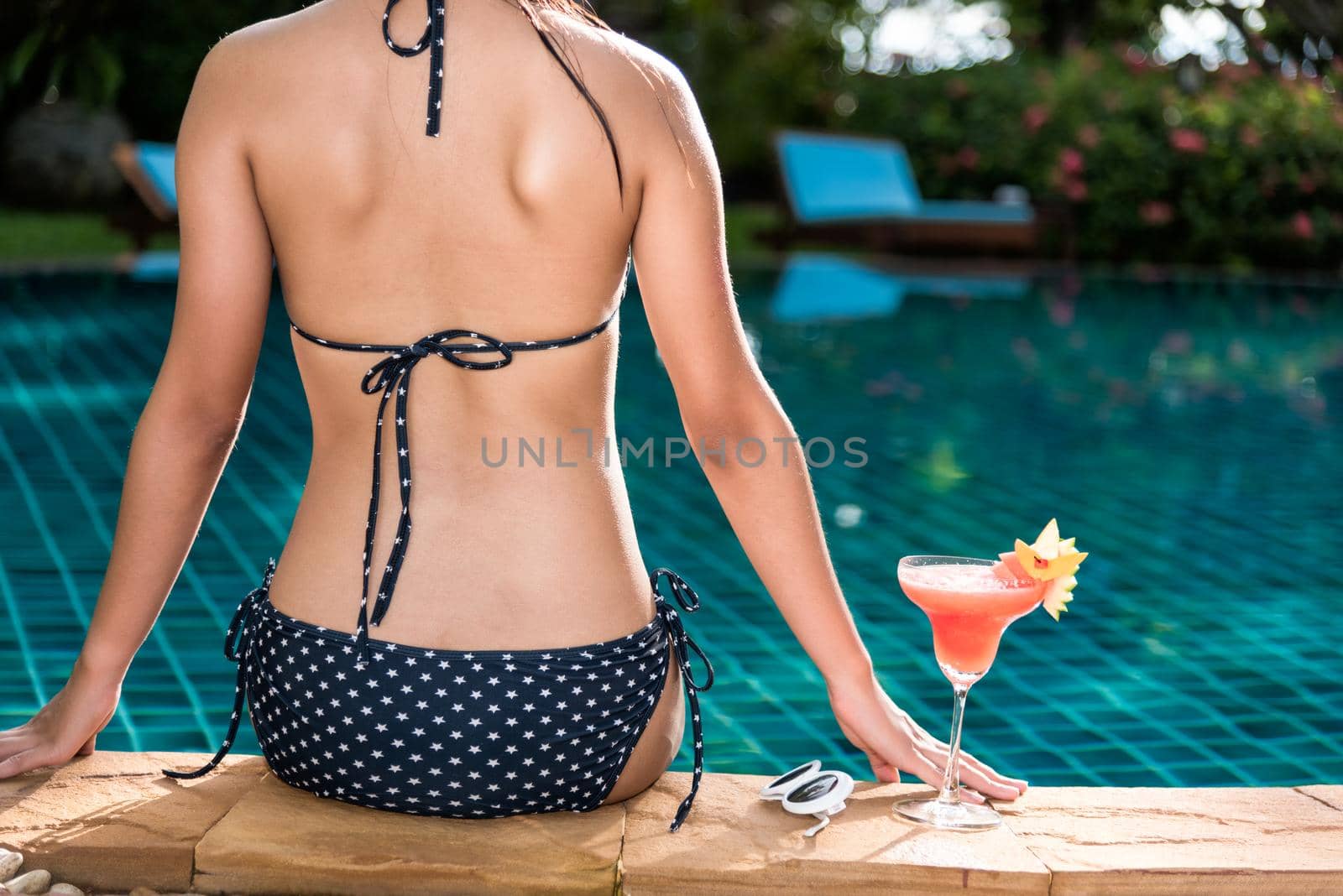 Beautiful Woman with cocktail glass near swimming pool blue water